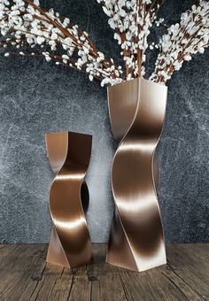 two metal vases sitting on top of a wooden table next to a flower arrangement