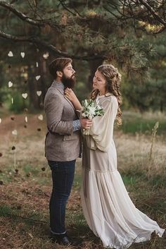 a man and woman standing next to each other in front of a tree with paper hearts