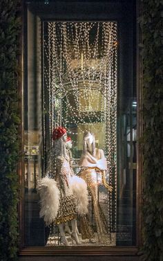 two mannequins dressed in gold and white with lights hanging from the ceiling