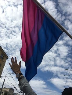 a person waving a rainbow colored flag on a street with buildings in the back ground