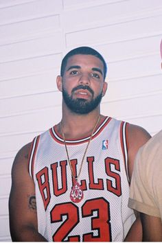 two men standing next to each other in front of a white wall and one wearing a pink hat