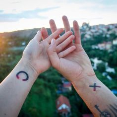 two people holding their hands up to each other with tattoos on them and the sky in the background