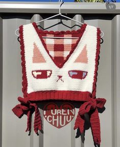 a red and white knitted sweater hanging from a clothes rack with sunglasses on it