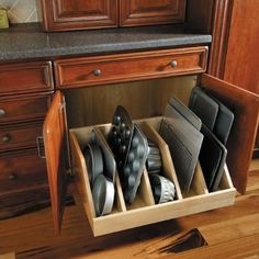 an open drawer in a kitchen filled with black and white dishes on top of wooden cabinets