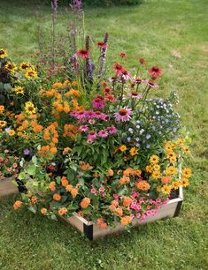 a wooden box filled with lots of colorful flowers on top of green grass covered ground