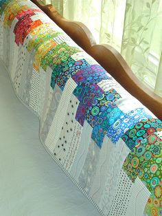 a bed with a quilt on top of it next to a wooden headboard and window