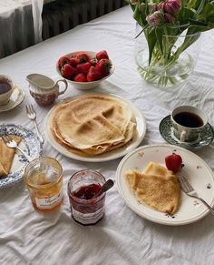 breakfast food is laid out on a table with flowers and fruit in the vases