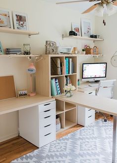 a desk with a computer on top of it in front of a ceiling fan and bookshelf