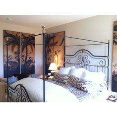 a bedroom with an iron bed frame and paintings on the wall behind it, along with two lamps