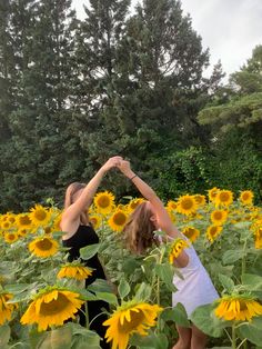 two women standing in a field of sunflowers with their hands up to the sky