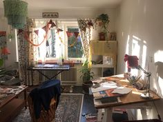 a cluttered living room with lots of papers on the table and plants in the window