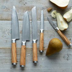 four knives are sitting next to an apple and pear