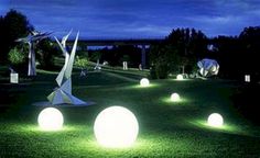 some white balls are in the grass and one is lit up by lights that look like origami birds