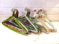 several pieces of colorful fabric hang from hooks on a white surface with wood planks in the background