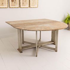 an old wooden table in a white room with three pictures on the wall behind it