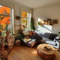 a living room filled with lots of furniture next to two large windows covered in fall foliage