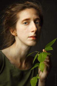 a woman holding a green leaf in her right hand and looking off to the side