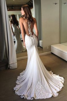 a woman in a white wedding dress looking at herself in the mirror with her back to the camera