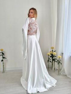 a woman in a white wedding dress standing next to flowers and looking off into the distance