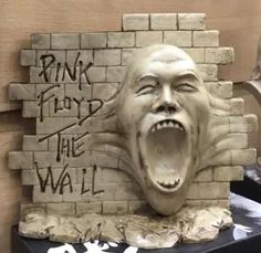 a statue of a screaming man with his mouth open next to a brick wall that says pink floyd the wall