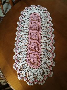 a pink and white crochet doily on a table with a wooden chair in the background