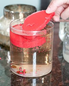 someone is dipping something into a glass with red liquid in it on a counter top