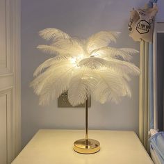 a lamp that is sitting on top of a table in front of a window with white feathers