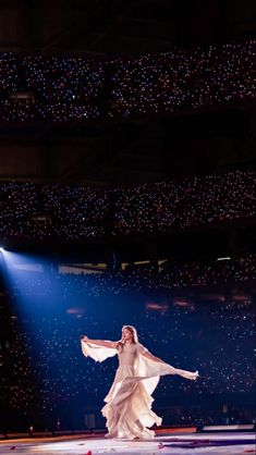 a woman in a white dress is dancing on the ice with lights behind her and snow flakes hanging from the ceiling