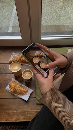 a woman sitting at a table with coffee and pastries in front of her phone
