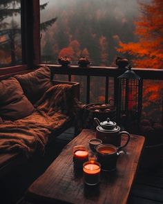 two cups of coffee on a table with candles in front of a window overlooking the woods