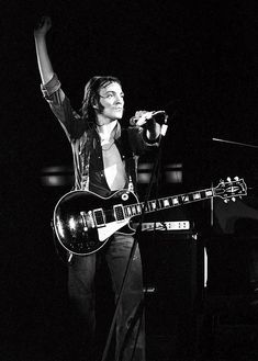 a man holding a guitar and singing into a microphone while standing next to a keyboard