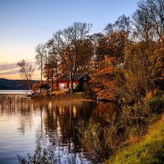 a house sitting on the shore of a lake surrounded by trees with fall foliage around it