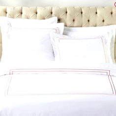 a bed with white linens and red trim on the headboard is pictured in this image