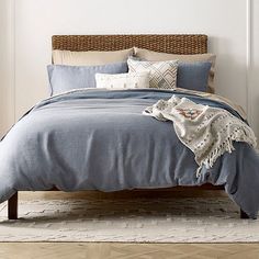 a bed with blue linens and pillows in a white walled room next to a window