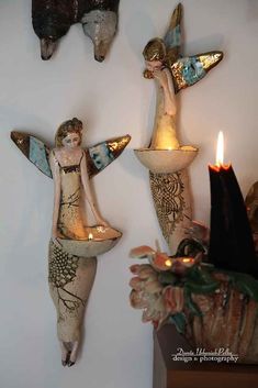 three ceramic angel figurines are hanging on the wall next to a lit candle