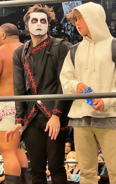 two men with face paint standing next to each other in front of a wrestling ring