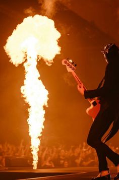 a man with a guitar standing in front of a large object that is on fire
