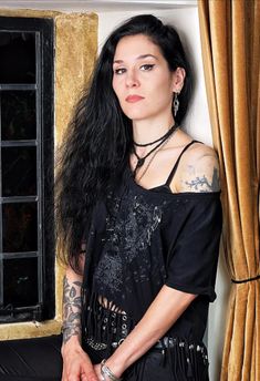 a woman with long black hair and piercings standing in front of a window looking at the camera