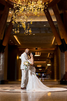 a bride and groom standing in the middle of a hall with flowers hanging from the ceiling