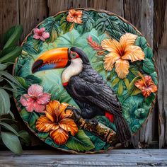 a plate with a toucan and flowers painted on the front is sitting against a wooden fence