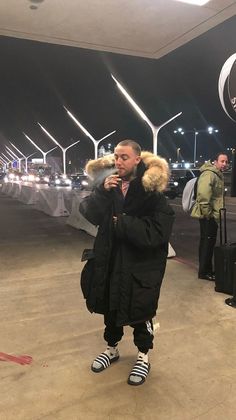 a man standing in front of an airport with his luggage and wearing a parka