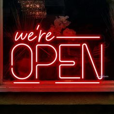 we're open neon sign on the side of a store front window with red lights