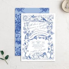 a blue and white wedding card on top of a table next to a flowery plant