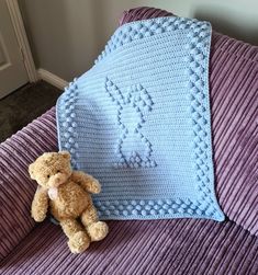 a teddy bear sitting next to a crocheted blanket