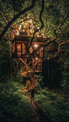 a person standing in front of a tree house with lights on it's roof