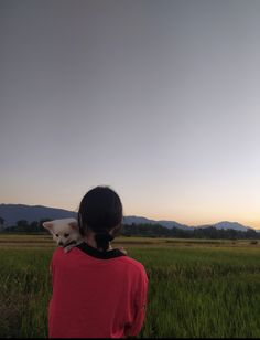 a person holding a dog in their arms while standing in a field with mountains in the background