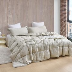 an unmade bed sitting in front of a brick wall and window with white pillows on it