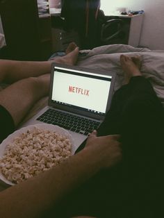 a person laying in bed with a plate of popcorn and a laptop on their lap