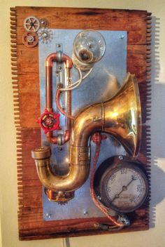 a wall mounted clock with brass pipes and a horn on the side, attached to a wooden board