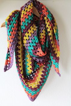 a multicolored crocheted scarf hanging from a hook on a white wall